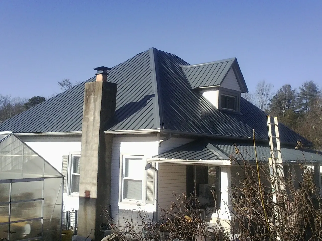 Dark blue standing seam metal roof on a white farmhouse with dormer — Slate & Tile Roof Repair by Roofing Brothers in Albuquerque