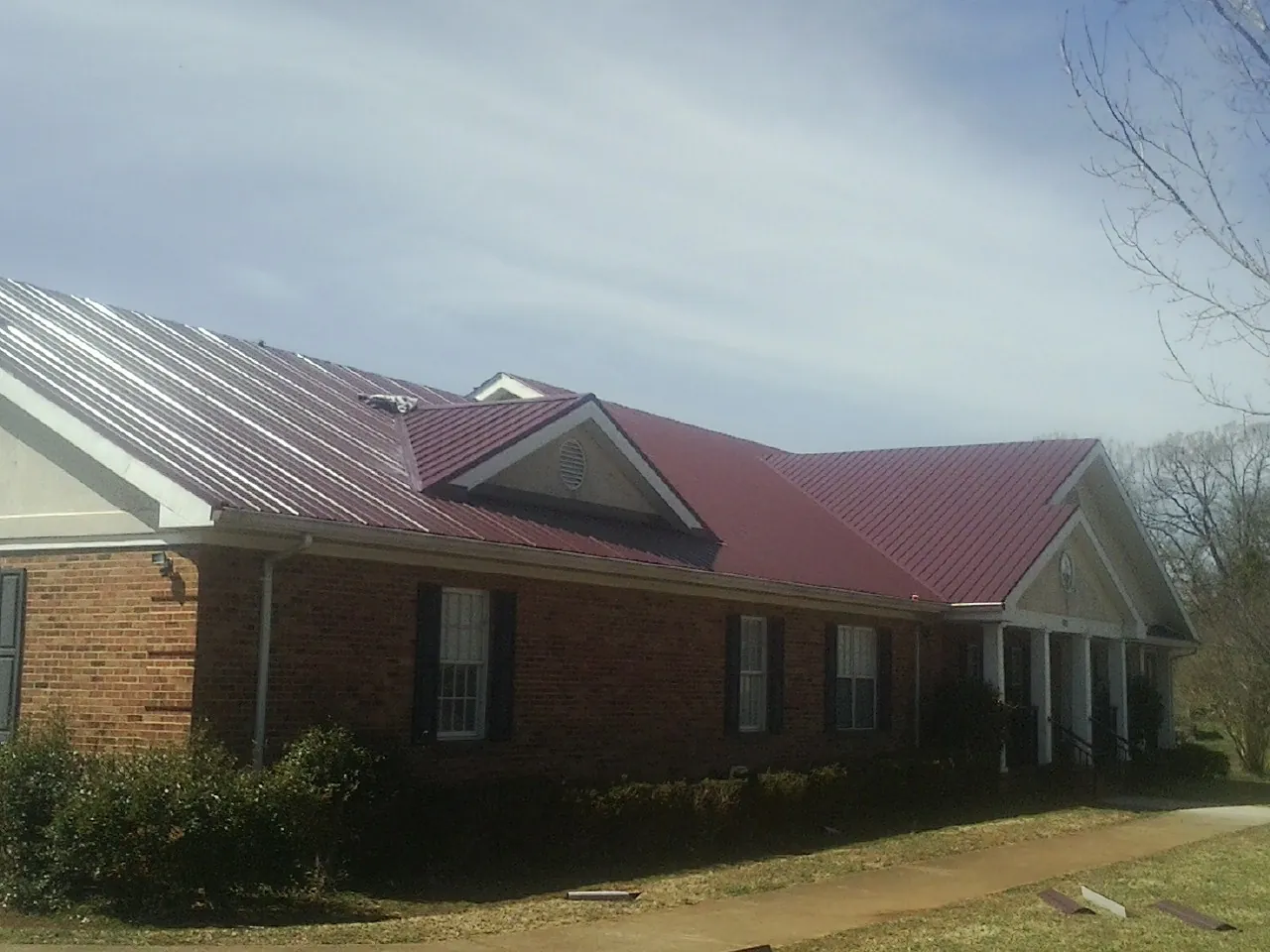 Red metal roof with gabled entries on a long brick building, from a Hail Damage Roof Repair job in Albuquerque