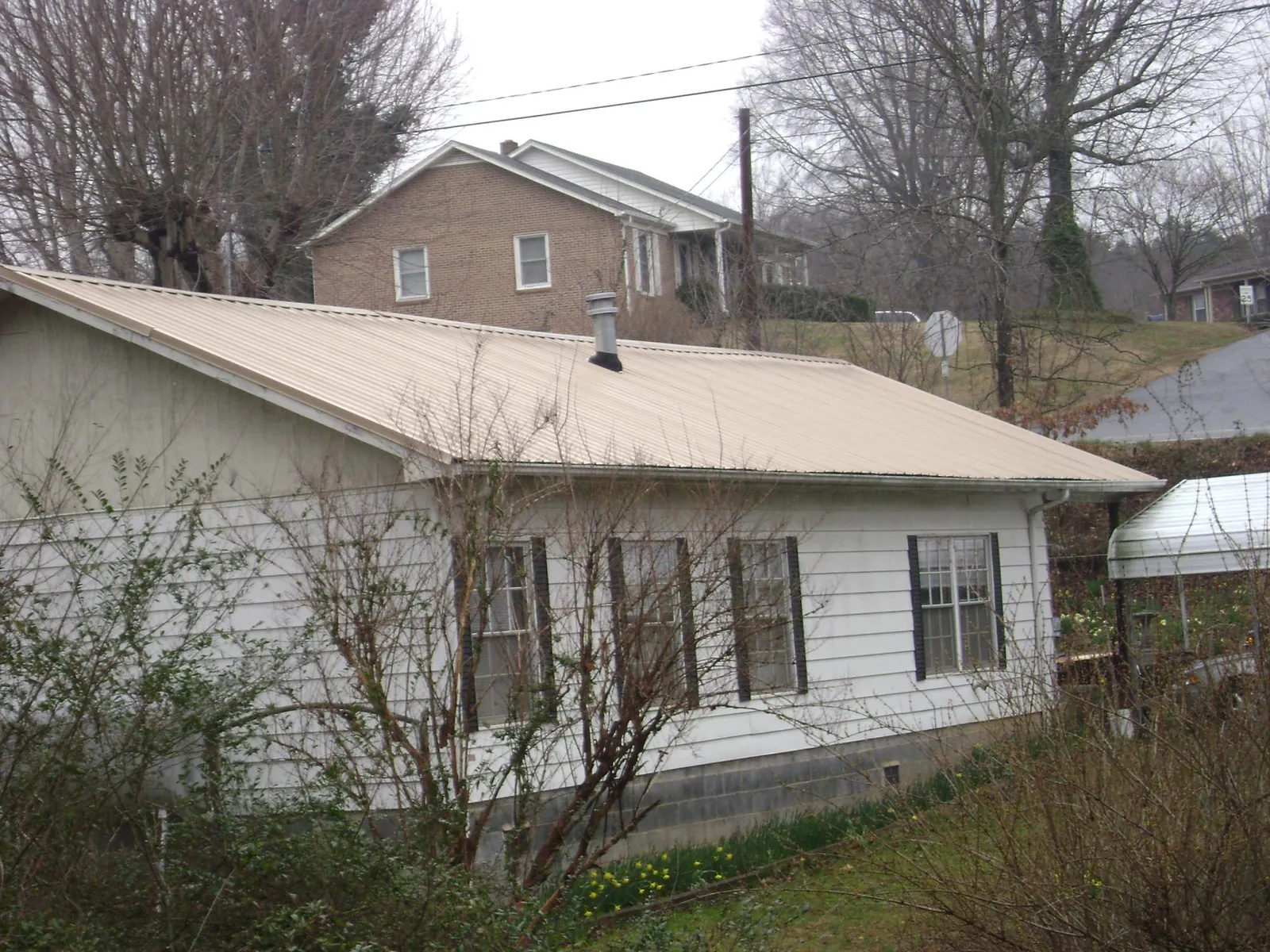 Tan metal roof on a white sided house set into a hillside — Commercial Roofing by Roofing Brothers in Albuquerque